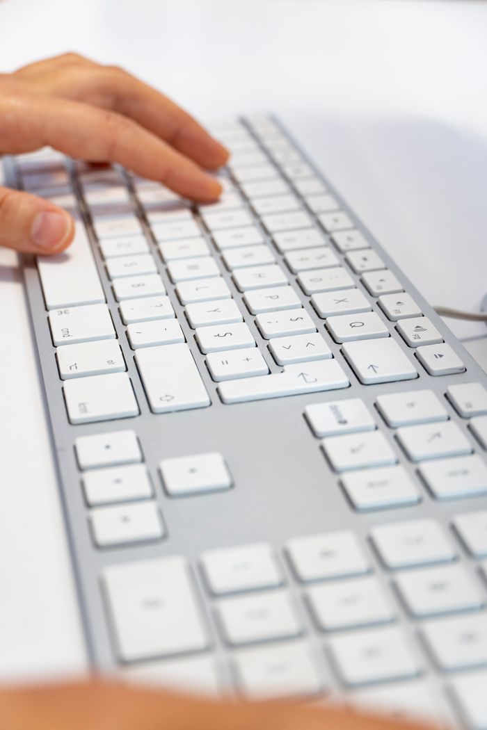 Services A person's hand typing on a sleek white wireless keyboard, in bright, natural light.