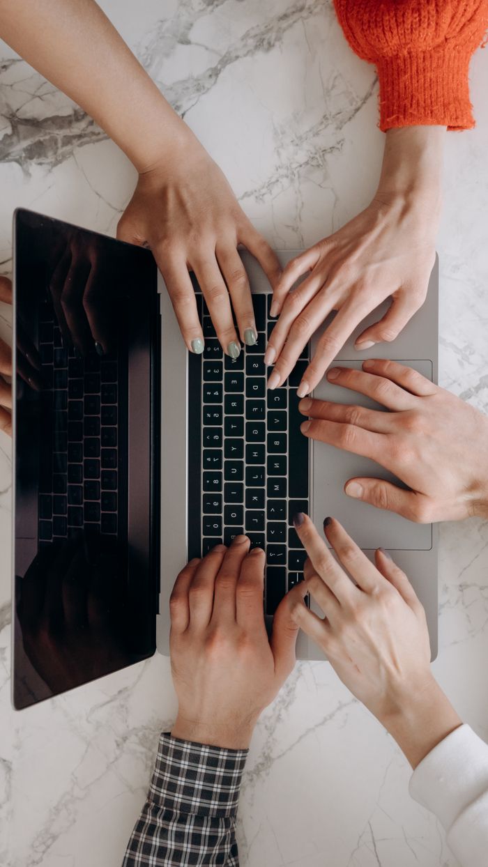 Services A top-down view of multiple hands typing on a laptop keyboard on a marble desk, indicating teamwork.
