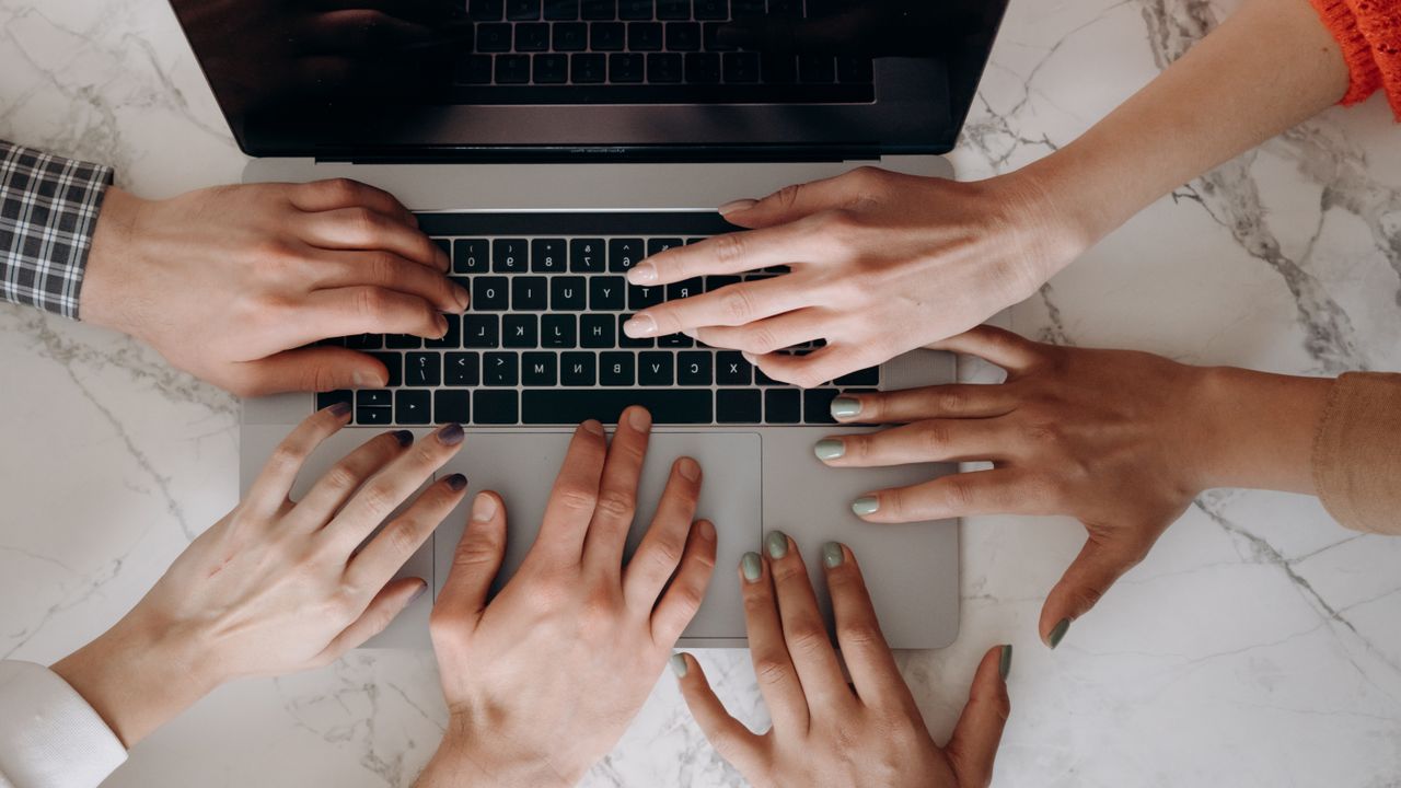 Services Top view of multiple hands typing on a laptop, showcasing teamwork and diversity.
