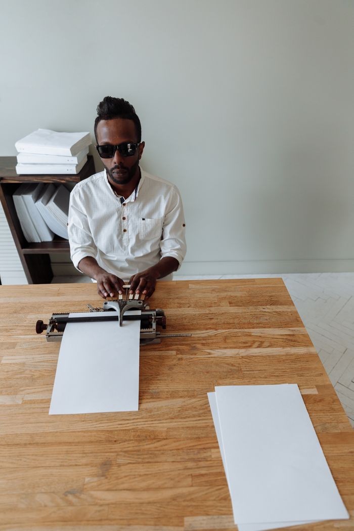 Services Blind man using a braille typewriter at a wooden desk inside a minimalistic room.