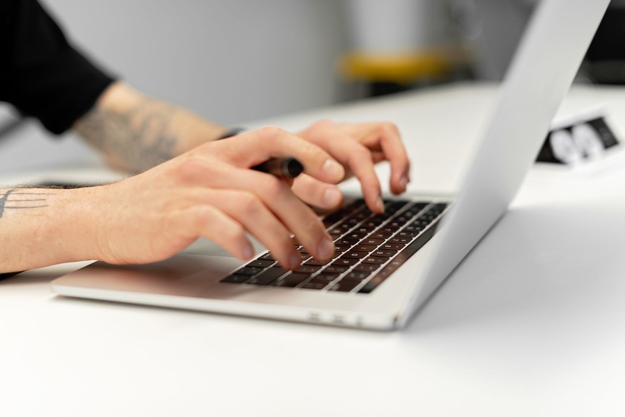 Services Close-up of tattooed hands typing on a laptop keyboard, showcasing productivity.