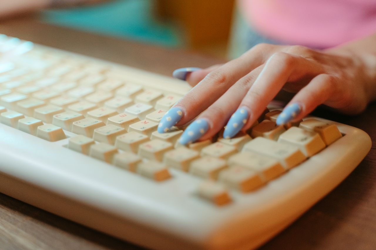 Services Closeup of a hand with polka dot nails typing on a vintage keyboard, emphasizing retro technology.